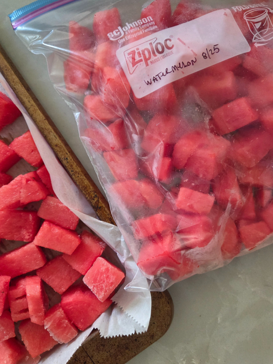 Frozen watermelon cubes in a labeled freezer bag next to a baking sheet