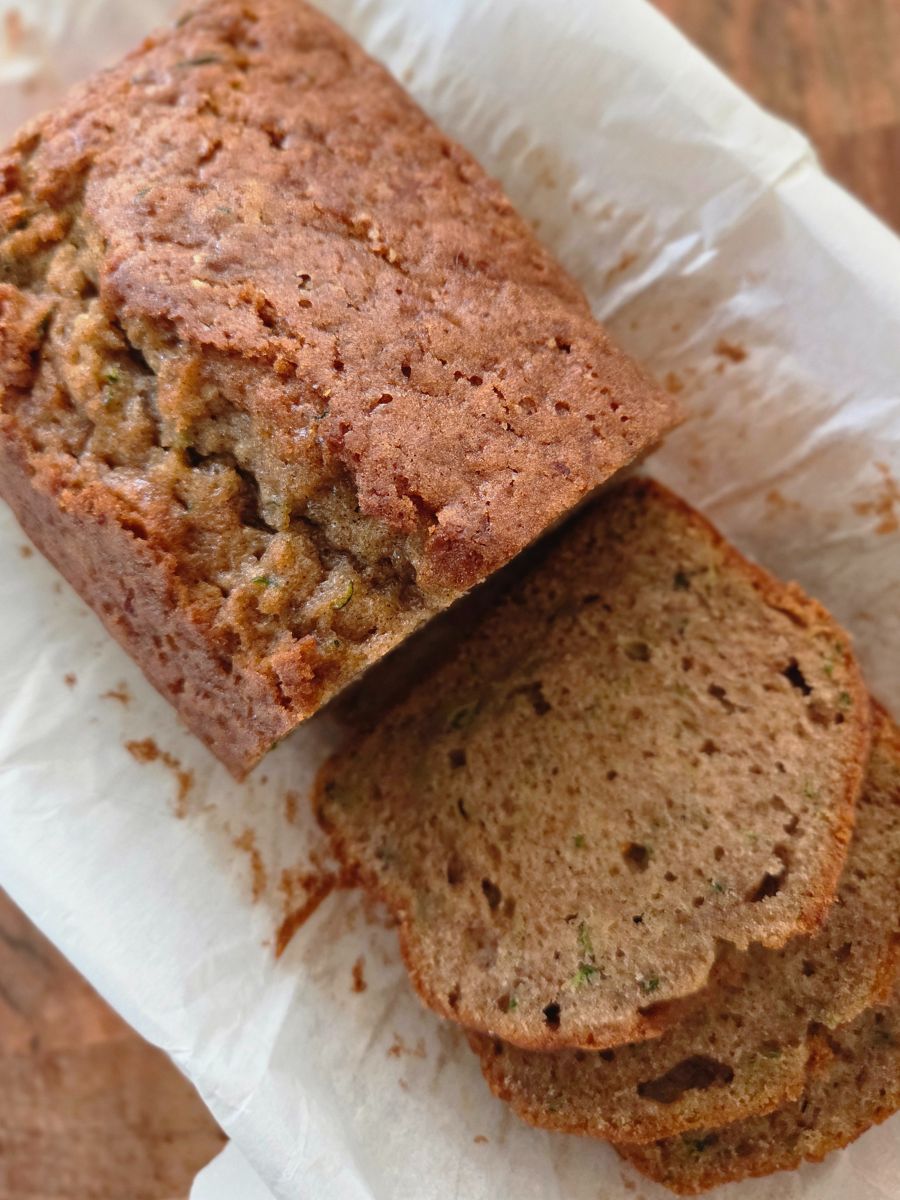 Freshly baked cinnamon zucchini bread loaf with a few slices cut, showing moist texture with zucchini flecks