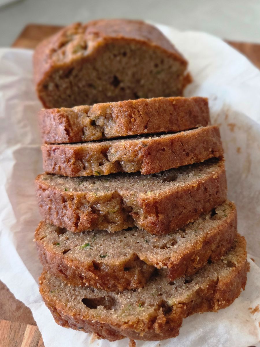 Stack of sliced cinnamon zucchini bread on parchment, moist and lightly spiced with cinnamon.
